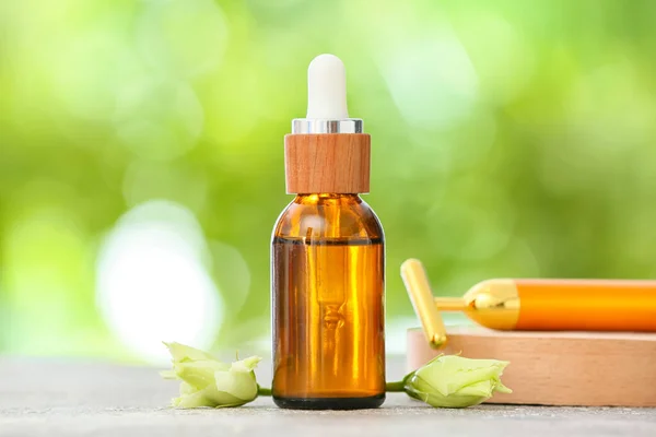 Bottle of essential oil and facial massager on table outdoors, closeup