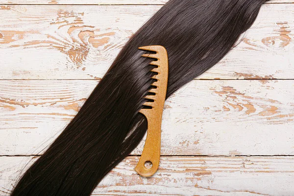 Hair strand and comb on light wooden background