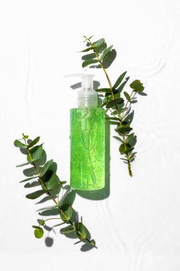 Beyaz arka planda bir şişe kozmetik ürünü ve okaliptüs dalları