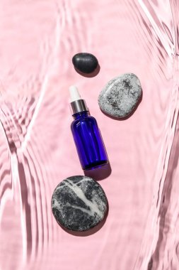 Renkli arka planda suda bir şişe kozmetik ürün ve taşlar