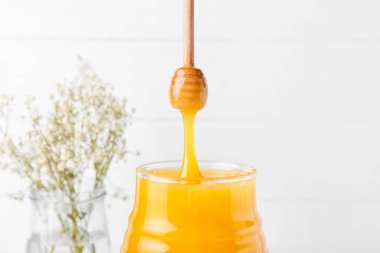 Aydınlatma arka planında camdan kavanoza dökülen bal, yakın plan