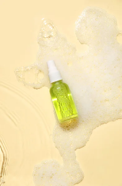 Bottle of cosmetic product in water with foam on color background