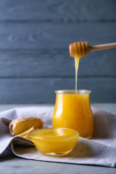 色の木製の背景にガラス瓶にディップから注ぐ蜂蜜 — ストック写真