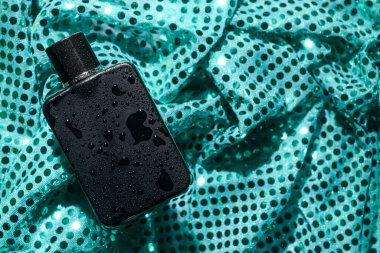 Kumaş zemininde su damlaları olan bir şişe parfüm.