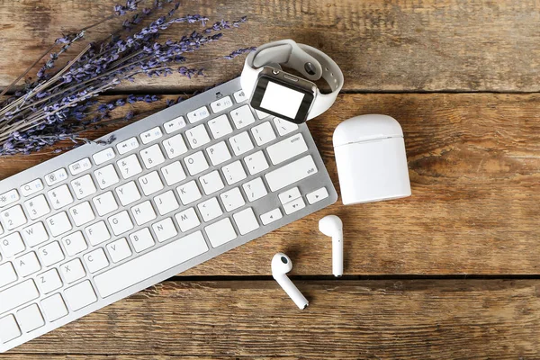 Modern earphones, computer keyboard, smart watch and lavender on wooden background