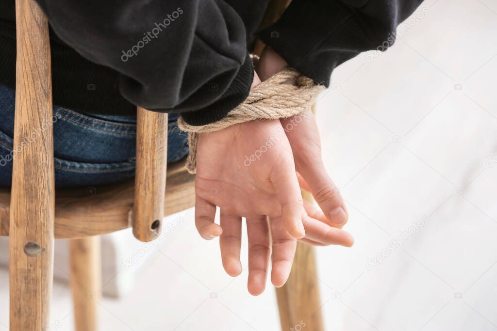 Female hostage with tied hands sitting on chair in room, closeup