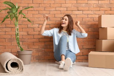 Anahtarı olan mutlu genç bir kadın yeni dairesinde yerde oturuyor.