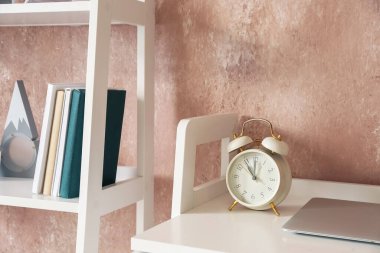 Masadaki çalar saat ve renkli duvarın yanındaki kitaplık.