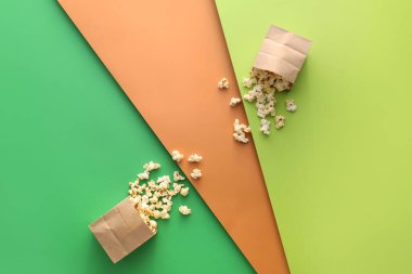 Renkli arkaplanda lezzetli patlamış mısır bulunan kağıt torbalar