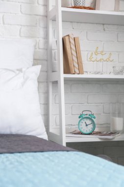 Tuğla duvarın yanında çalar saati olan bir kitap rafı.