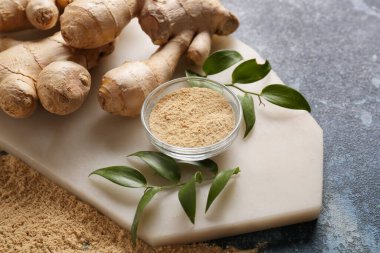 Zencefil tozu ve arkaplanda taze kökler olan kase.