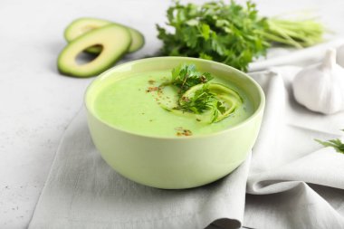 Açık arkaplanda yeşil gazpacho, avokado ve maydanozlu kase