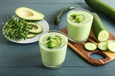 Yeşil gazpacho ve ahşap arkaplanda bulunan malzemeli bardaklar.