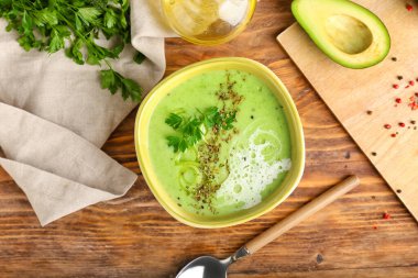 Yeşil gazpacho ve ahşap arka planda malzemelerle dolu bir kase.