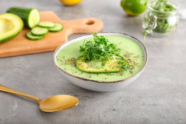 Yeşil gazpacho ve gri arka planda malzemelerle dolu bir kase.
