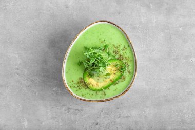 Gri arkaplanda yeşil gazpacho olan kase.