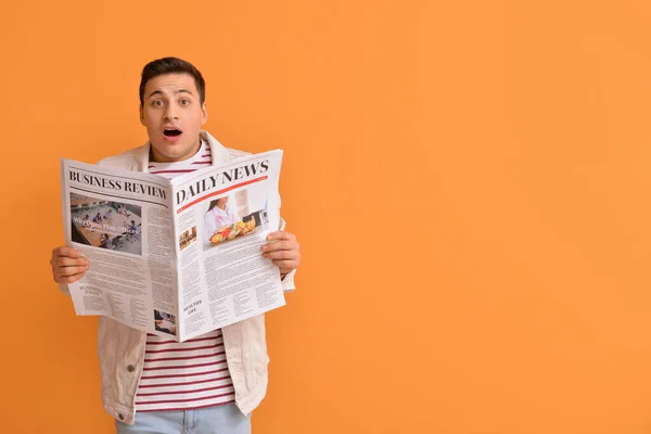 Shocked young man with newspaper on color background