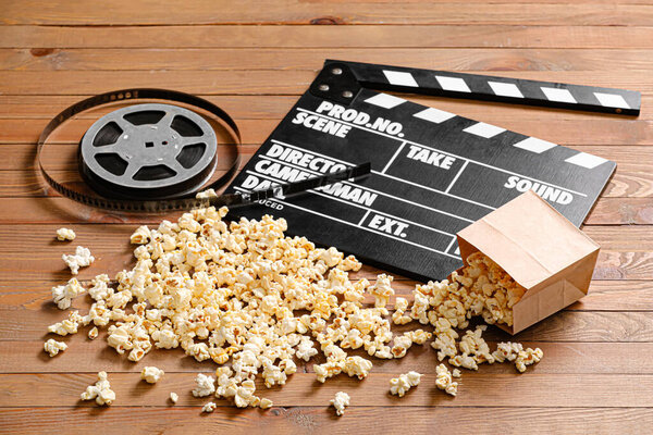 Tasty popcorn with movie clapperboard and reel on wooden background