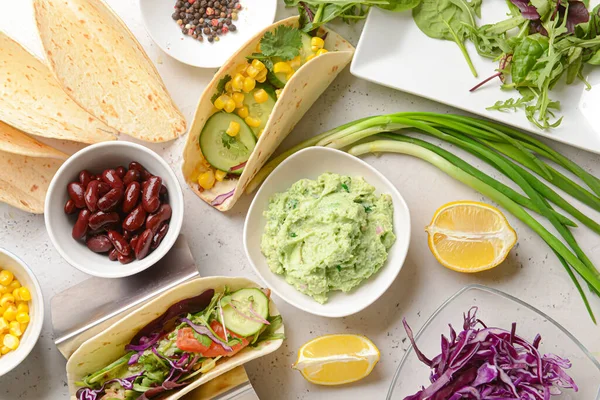 Composition with tacos and tasty guacamole in bowl on light background