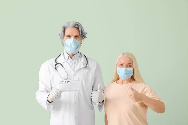 医師と色の背景に親指アップを示すワクチンの国際証明書を持つ患者 — ストック写真