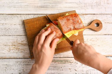 Hafif ahşap arka planda lezzetli sandviç kesen bir kadın.