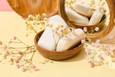 Arkaplanda sabun barları, çiçekler ve ayna olan kase