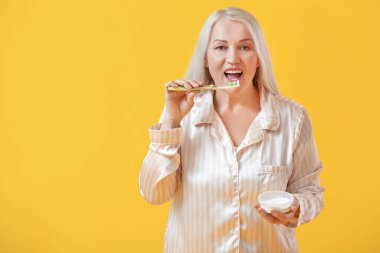 Renkli arka planda dişlerini fırçalayan olgun bir kadın.