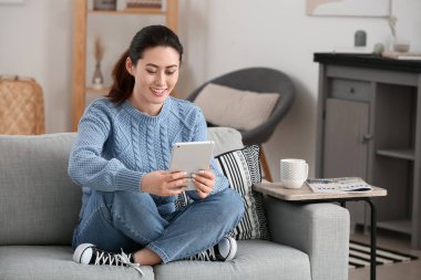 Evde tablet bilgisayar kullanan genç bir kadın.