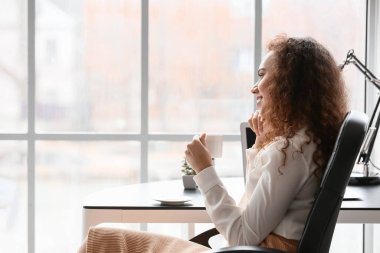 Güzel genç bayan ofiste kahve içiyor.