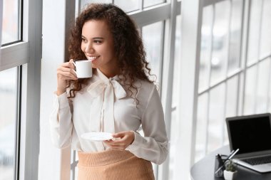 Güzel genç bayan ofiste kahve içiyor.
