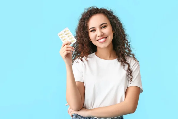 Young woman with fish oil pills on color background