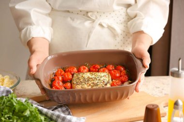 Mutfakta fırında domates ve peynir taşıyan bir kadın.