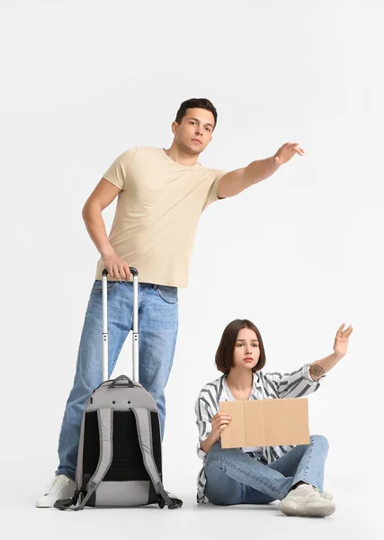 带硬纸板和手提箱的年轻夫妇在浅色背景下搭便车 — 图库照片