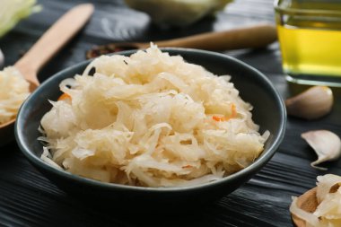 Koyu ahşap arka planda lezzetli lahana turşulu kase, yakın plan.