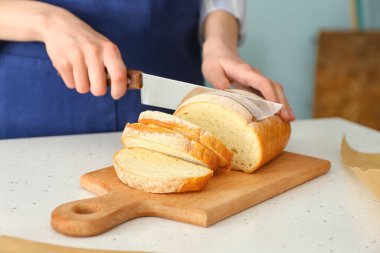 Kadın aşçı mutfak masasında taze ekmek kesiyor, yakın plan.
