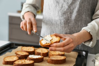 Kadın aşçı, mutfak masasında peynirli tost hazırlıyor.