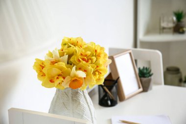 Beyaz duvarın yanındaki masada güzel narsisus çiçekleri.