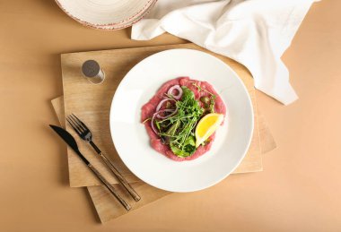 Lezzetli dana carpaccio tabağı ve renkli arka planda çatal bıçak takımı.