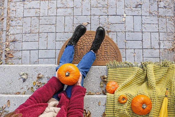 Woman with pumpkins sitting near entrance of house on autumn day