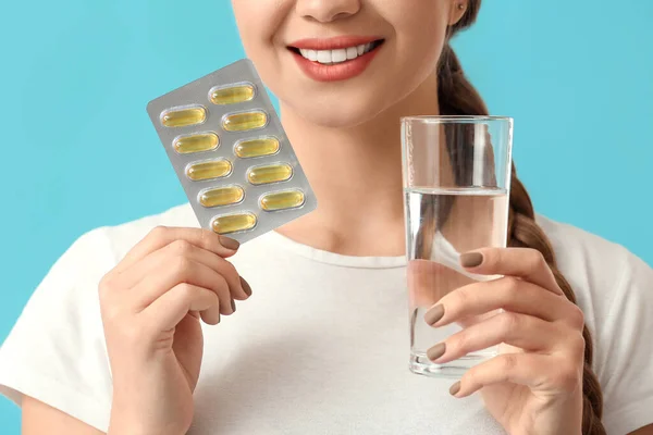 Young woman with fish oil on color background, closeup