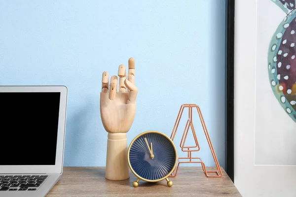 Wooden hand and clock on table near color wall