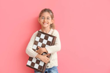 Cute little girl with chessboard on color background clipart