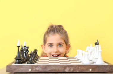 Cute little girl playing chess on color background clipart