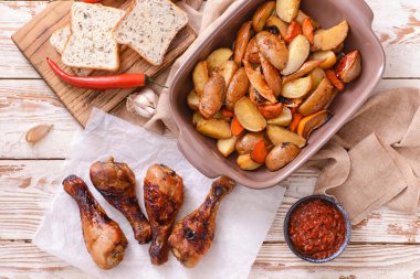 Kızarmış tavuk budu ve hafif ahşap arka planda fırında patates.