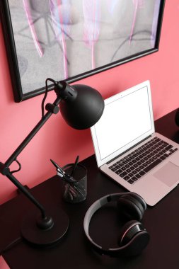 Renk duvarının yanında dizüstü bilgisayarı ve kulaklığı olan modern bir işyeri