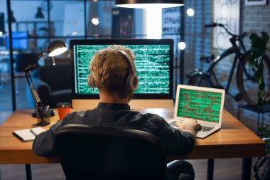Genç programcı geceleri bilgisayar ve dizüstü bilgisayarla çalışıyor.