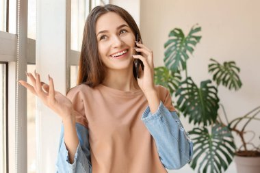 Evde cep telefonuyla konuşan güzel genç bir kadın.