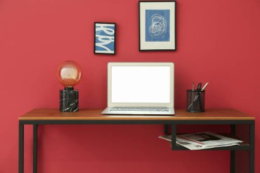 Renk duvarının yanında dizüstü bilgisayarı ve lambası olan modern işyeri