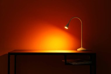 Parlayan lamba ve gazeteler karanlık odada masanın üstünde.