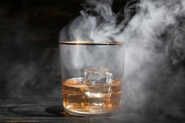 Bir bardak soğuk viski ve siyah ahşap arka planda duman.